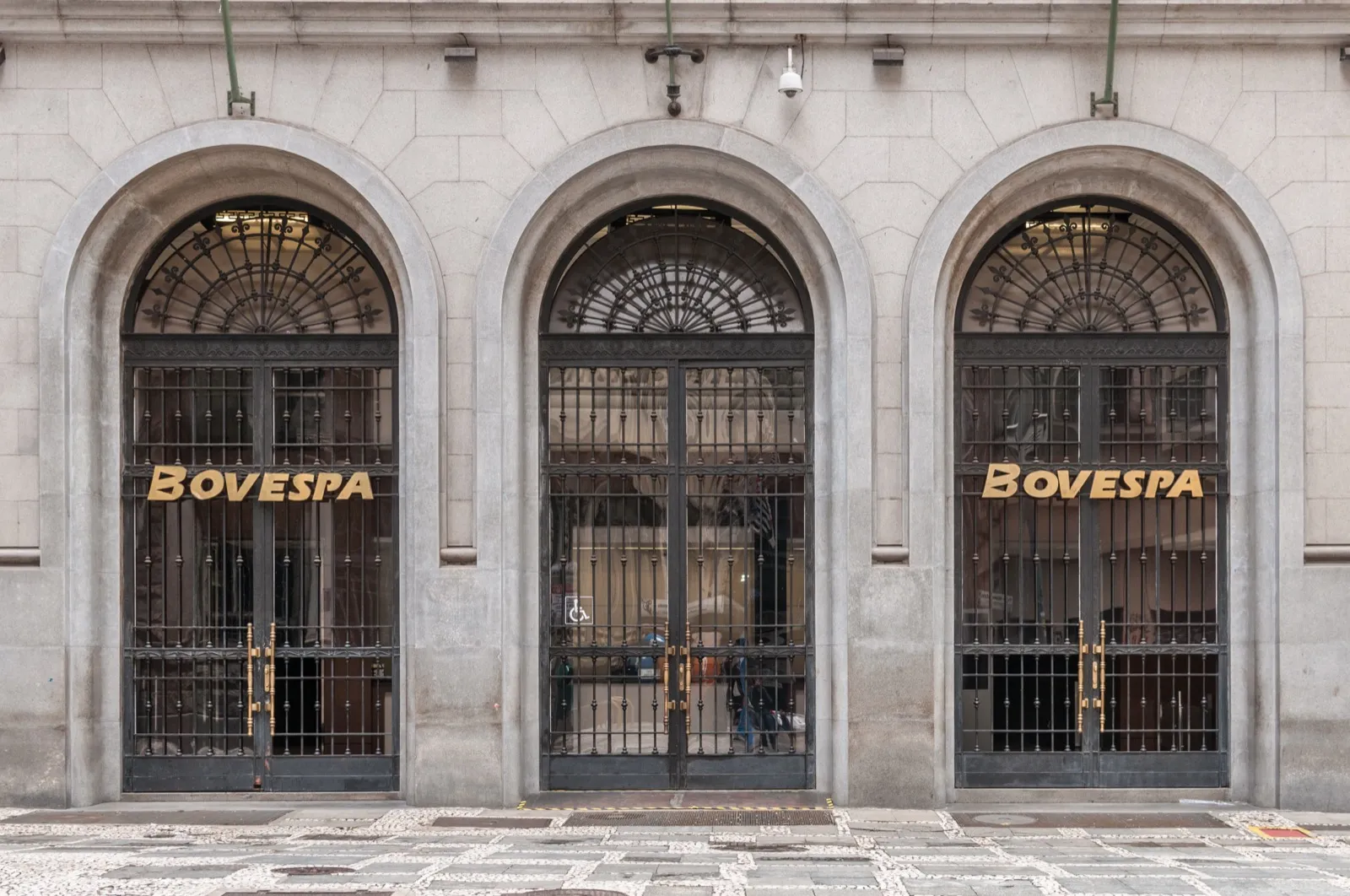 Fachada da Bolsa de Valores de São Paulo, com três portas de ferro em arco e as letras BOVESPA em dourado