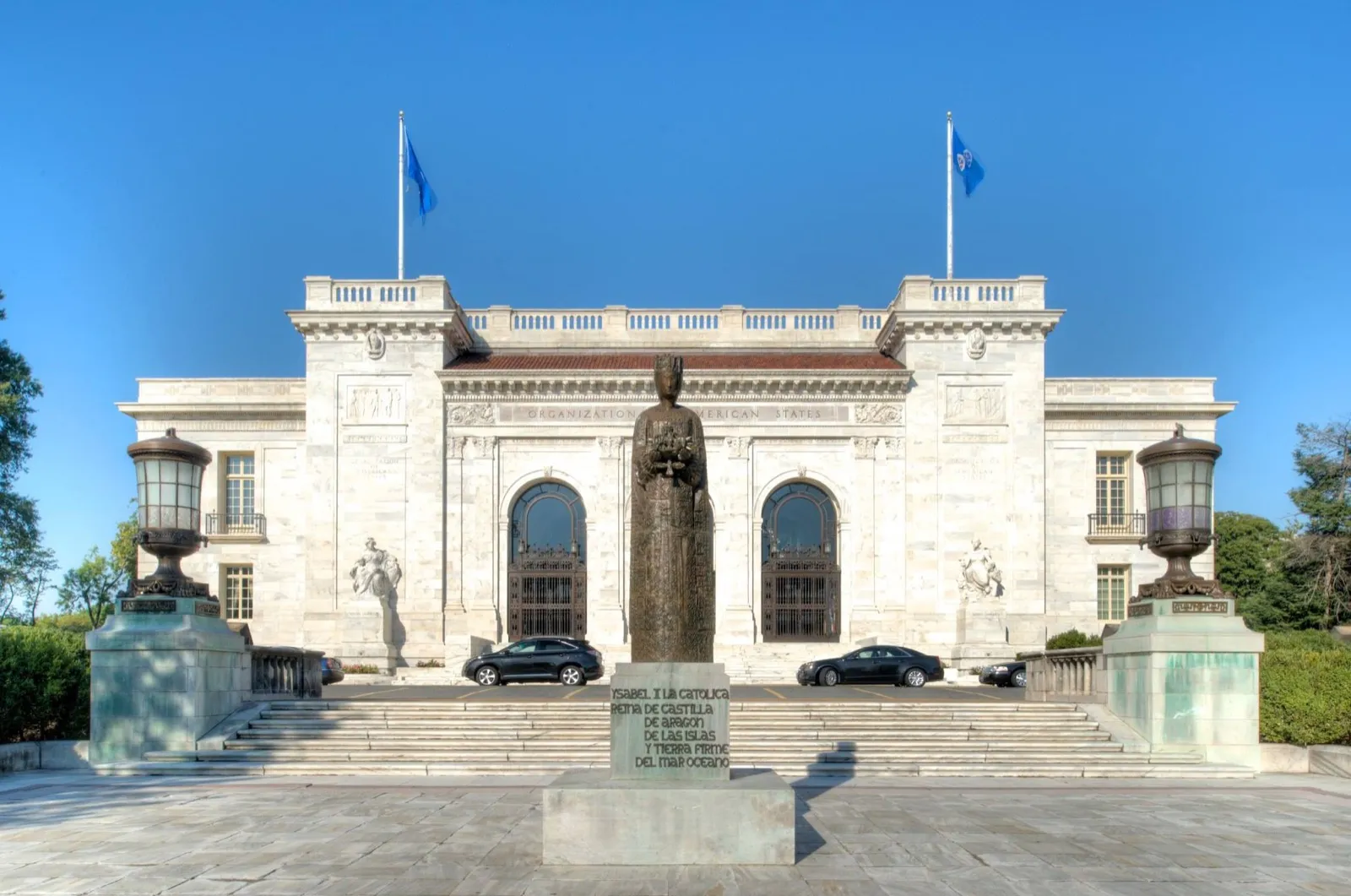 Fachada de mármore branco do edifício da Organização dos Estados Americanos, com duas bandeiras azuis e uma estátua na entrada