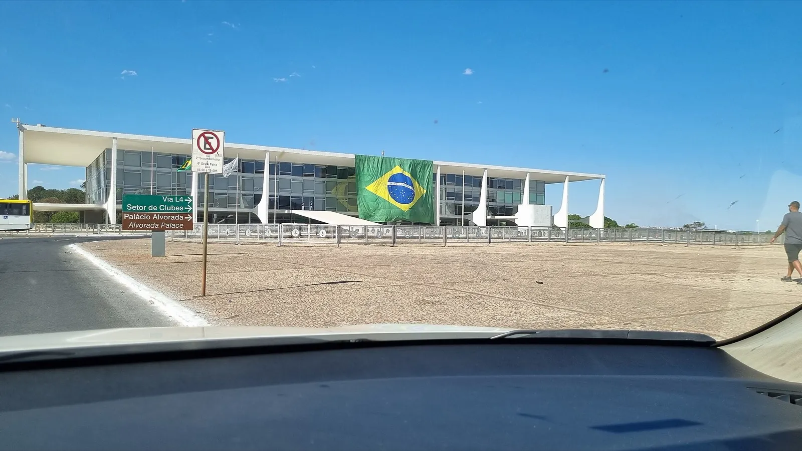 Bandeira do Brasil grande, pendurada na fachada do Palácio do Planalto, em Brasília, vista através do para-brisa de um carro
