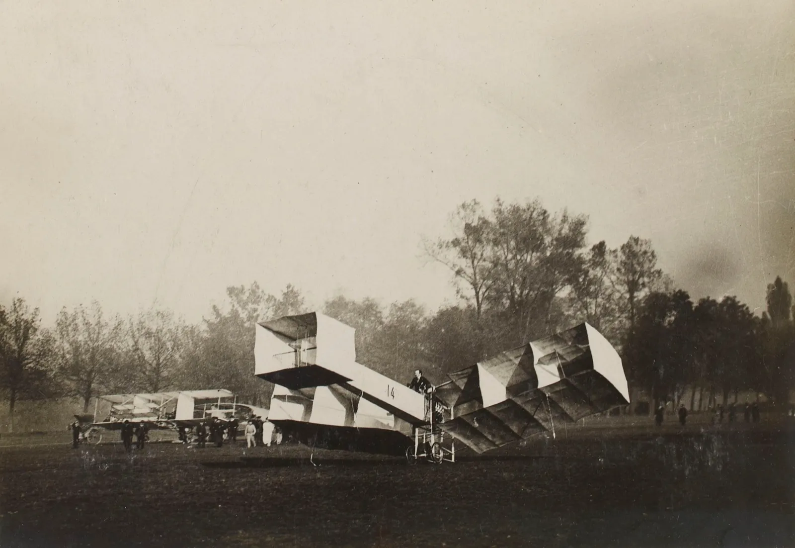 Fotografia antiga do 14-Bis de Santos Dumont, aeroplano de asas em células, com o Blériot IV ao fundo