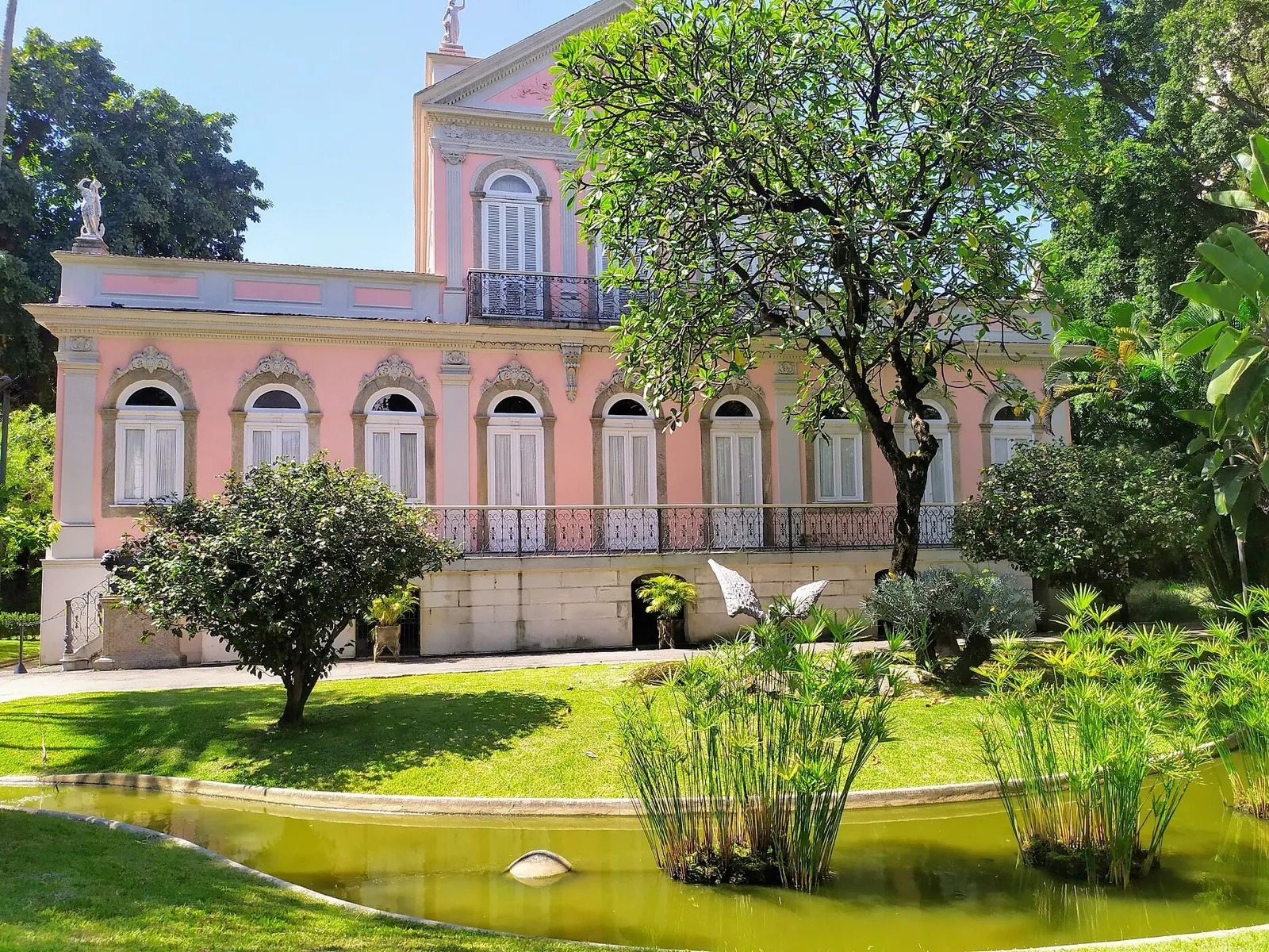 Fachada cor-de-rosa da Casa de Rui Barbosa, no Rio de Janeiro, cercada por jardim e espelho d'água