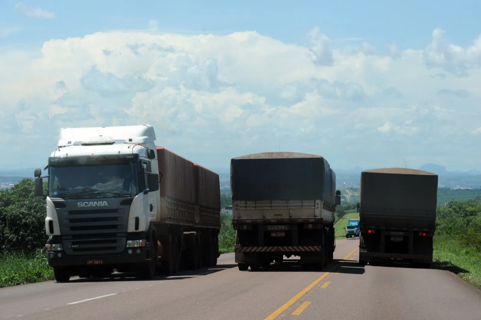 Três caminhões carregados com grãos trafegam em rodovia de pista dupla, sob céu com nuvens, perto de Rondonópolis (MT)