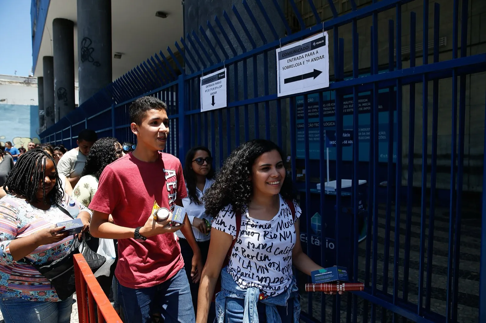 Estudantes caminham em fila diante de um portão azul de universidade no centro do Rio de Janeiro, em dia de prova do Enem