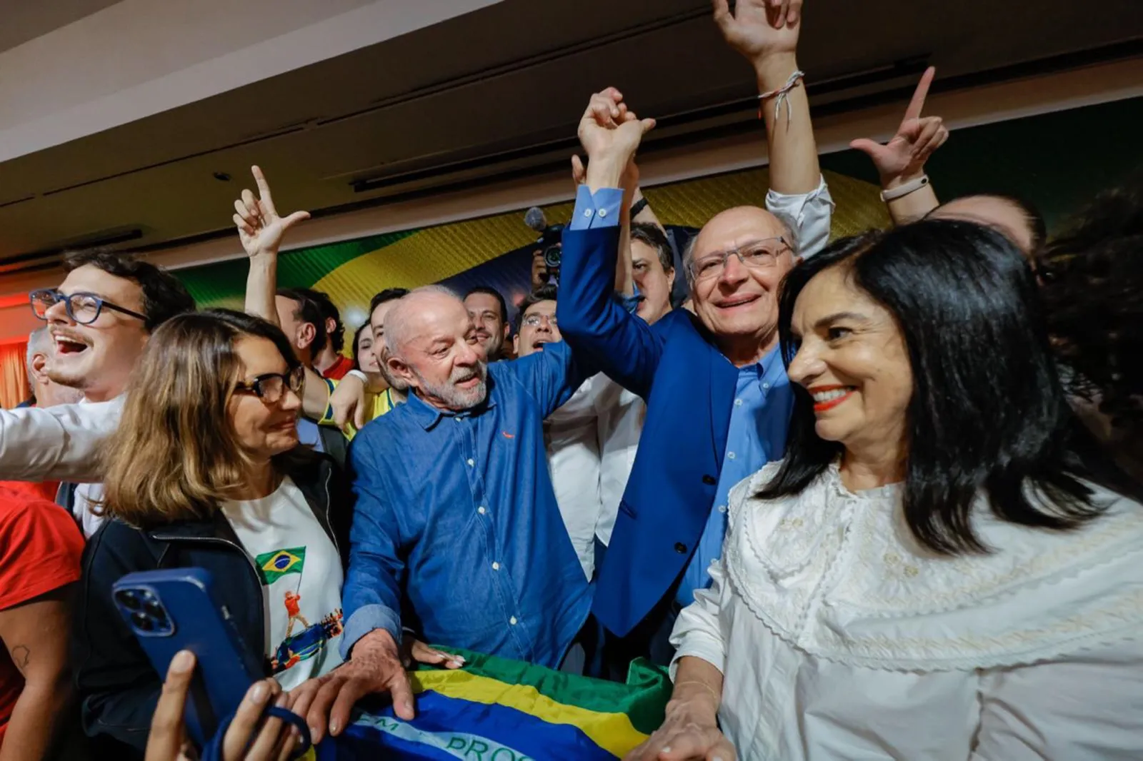 Lula e Geraldo Alckmin erguem as mãos unidas entre apoiadores e uma bandeira do Brasil