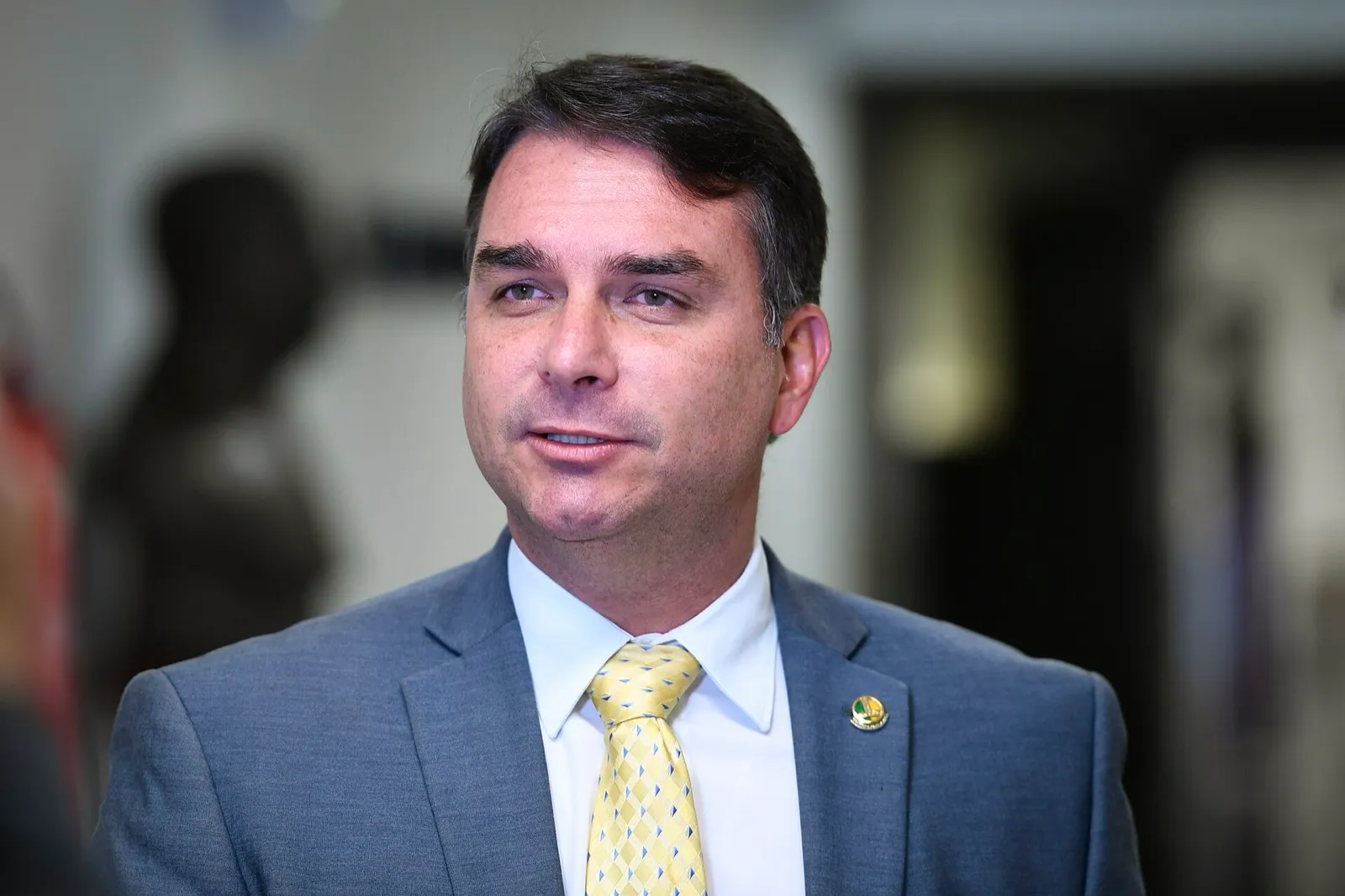 O senador Flávio Bolsonaro, de terno cinza e gravata amarela, fala durante entrevista
