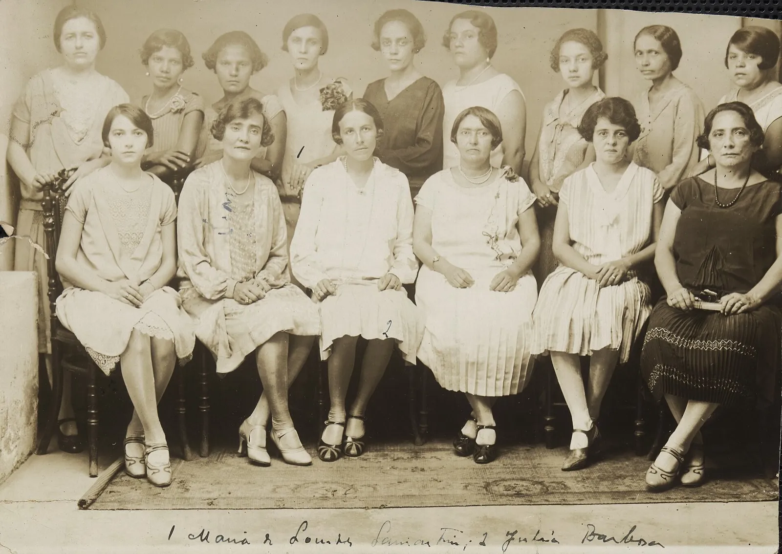 Grupo de 15 mulheres, sentadas e em pé, em retrato de estúdio, com nomes escritos à mão no rodapé da foto