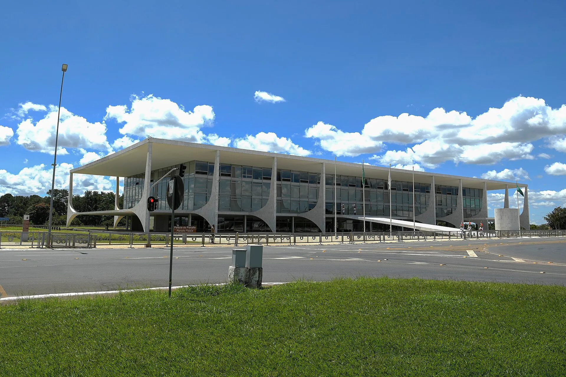 Fachada de concreto do Palácio do Planalto, em Brasília, sob céu azul com nuvens e bandeiras nos mastros