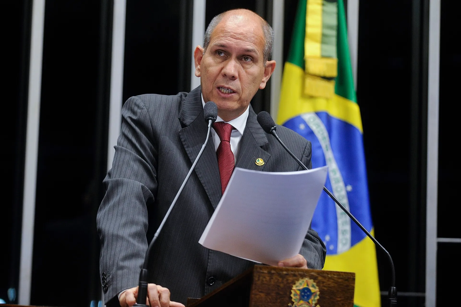Senador discursa no púlpito do Plenário do Senado Federal, com a bandeira nacional ao fundo